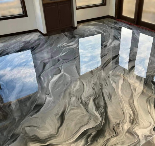 Glossy, marbled black and gray concrete floor reflecting outside sky and windows, creating an elegant, fluid appearance.