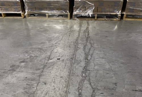 Warehouse floor with cracked concrete, surrounded by plastic-wrapped pallets on wooden bases in the background.