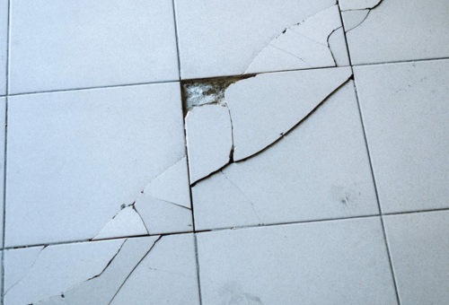 Cracked concrete floor tiles with a noticeable deep fracture running diagonally, exposing underlying material.