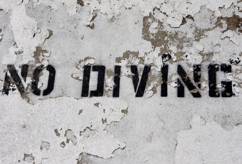"No Diving" stenciled in black on weathered, peeling concrete surface.