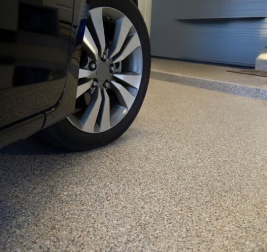 Car parked on speckled concrete garage floor with visible tire and detail of the textured surface.