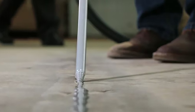 Applying sealant along a crack in a concrete floor, close-up of nozzle and shoes in the background.