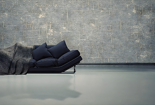 Modern room with a blue couch covered by a gray blanket, set against a textured concrete wall, on a smooth concrete floor.