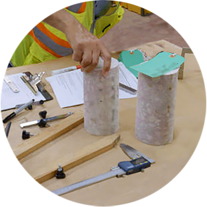 Worker examines cylindrical concrete samples on a table with calipers and notes.